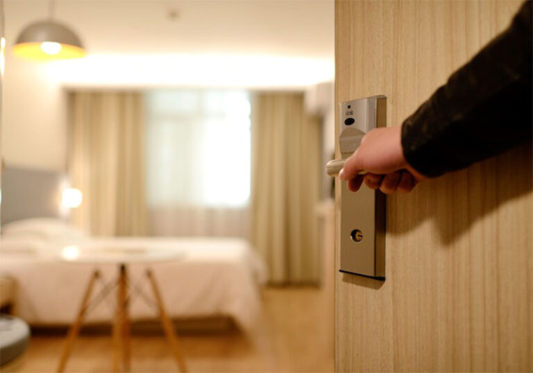 man arms opening a hotel room door, hotel bed and window in the background