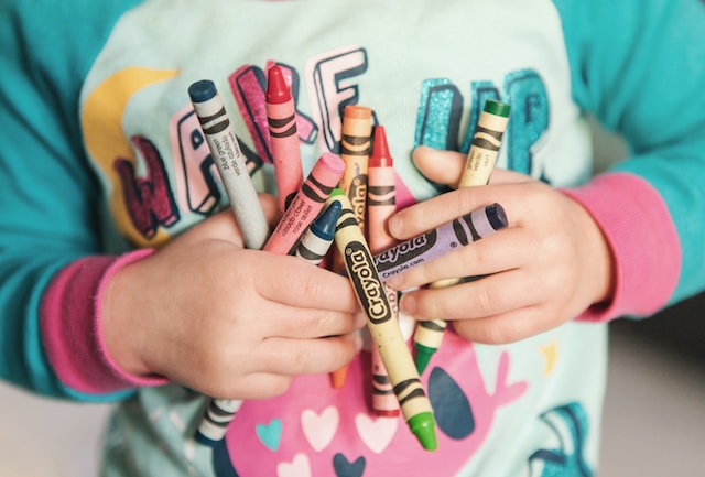 toddler holding a handful of colorful crayons